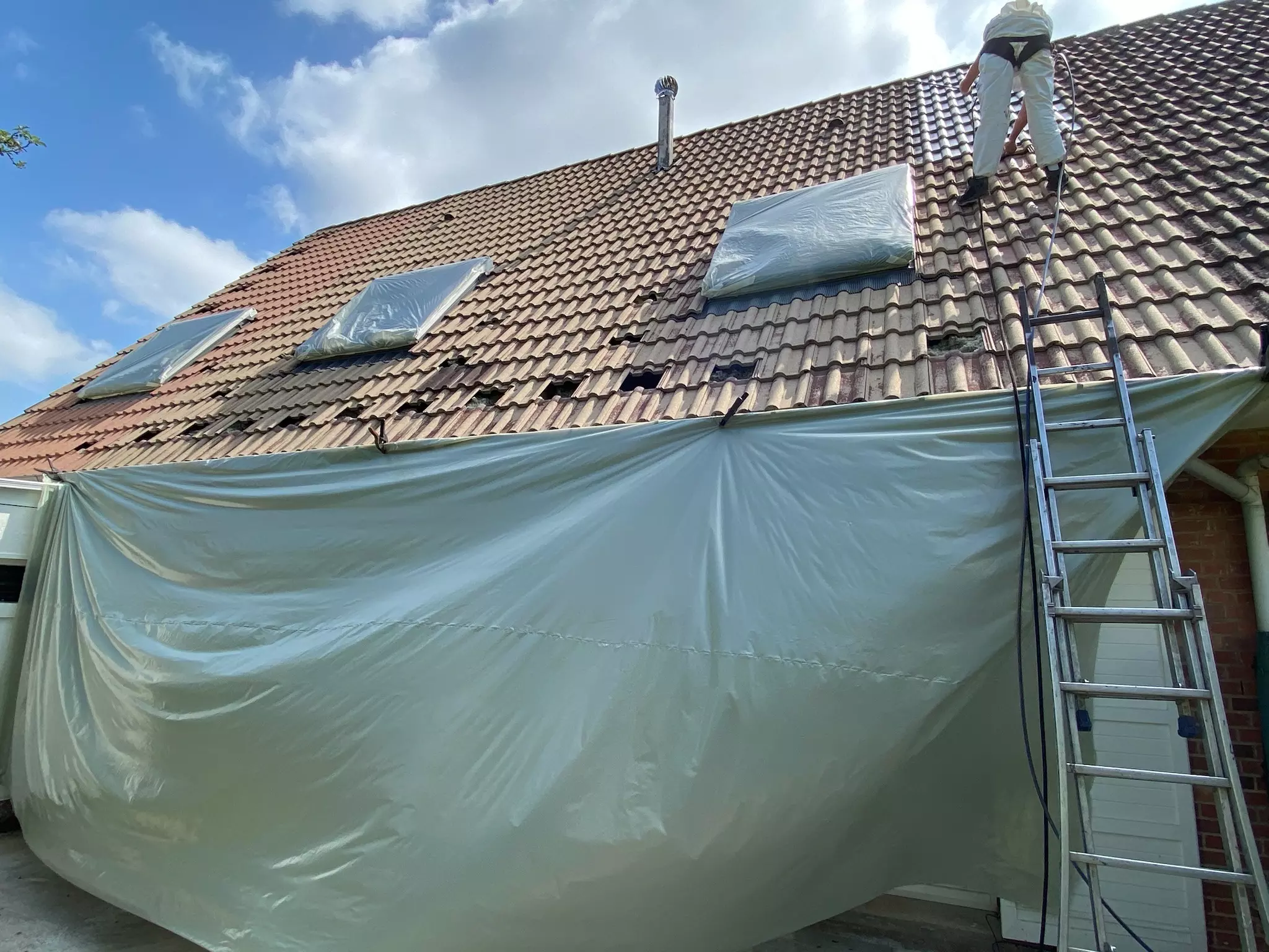 Artisan en train de travailler sur la rénovation d'une toiture bachée et parfaitement protégée